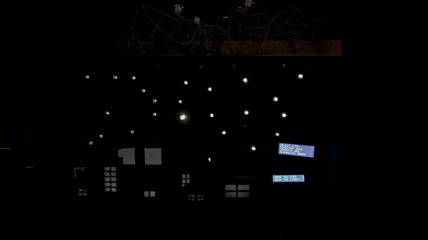 The installation running: the star field above the model neighbourhood with the city select menu on the LCD